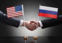 Two people shaking hands beneath US and Russian flags