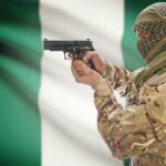 Camouflaged soldier aiming pistol near Nigerian flag