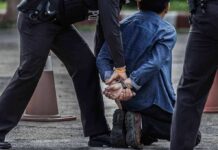 Person handcuffed by police officers on street kneeling