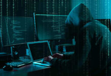 Hacker in dark room surrounded by computer screens