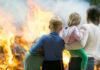 Three children and adult watching large fire outdoors