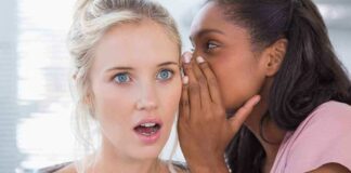 Two women in a casual setting, one whispering to the other who looks surprised