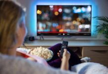 Person sitting on a couch watching a movie on a TV with popcorn in hand