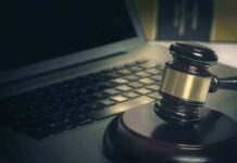 A gavel resting on a wooden block next to a laptop