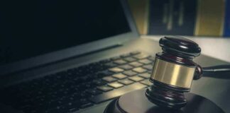 A gavel resting on a wooden block next to a laptop