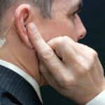 Top Secret Service Chief’s Brazen Self-Bonus Unveiled Man wearing an earpiece, touching his ear.