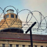 $2 Billion Detention Camp Mystery Deepens Barbed wire in front of a prison tower.