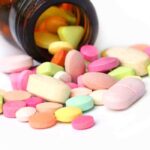 A variety of colorful pills and tablets spilled from a brown medicine bottle