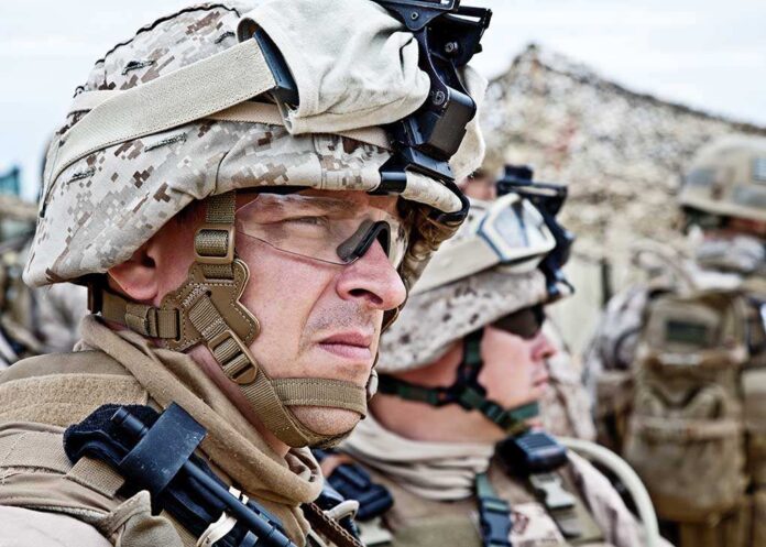 Two soldiers in military gear looking serious in an outdoor setting