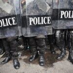 Police officers in riot gear standing behind shields marked 'POLICE'