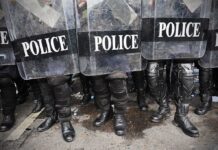 Police officers in riot gear standing behind shields marked 'POLICE'