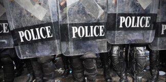 Police officers in riot gear standing behind shields marked 'POLICE'