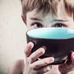 Gaza Famine Declared: Shockwaves Hit Global Stage A child with a serious expression holding a bowl close to their face