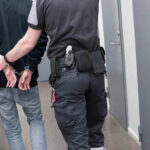Officer escorting handcuffed person down hallway.