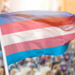 Trans Gun BAN Proposal – Is This CONSTITUTIONAL? Transgender pride flag waving at outdoor event.