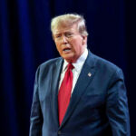TRUMP vs FED CHAIR: Chaos Erupts Over Rate War! Man in suit with red tie speaking on stage.
