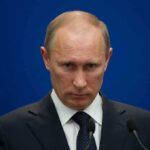 BIPARTISAN BILL Targets Putin’s Kidnapping SCANDAL A serious-looking man in a suit at a press conference with a blue background