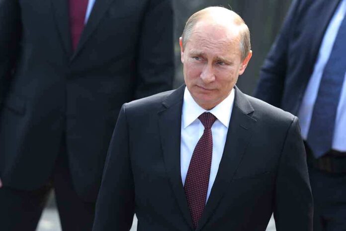 A serious-looking man in a suit walking outdoors with security personnel in the background