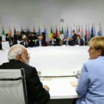 People seated around a large round table, flags behind.