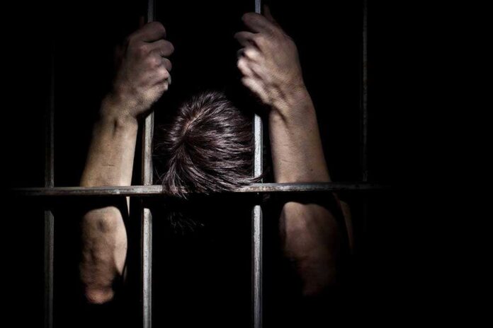 Hands gripping prison bars in a dark setting