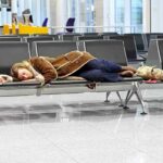 Holiday Travel CHAOS Looms: Airlines ISSUE WARNING! A traveler sleeping on a bench in an airport waiting area