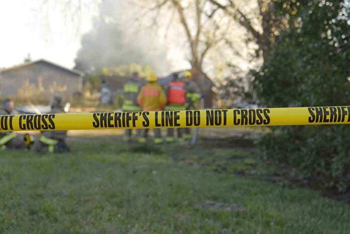 Yellow police tape marking a restricted area at a fire scene with firefighters in the background