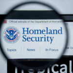 Chaos Erupts Across U.S After ICE Shooting Magnifying glass showing Homeland Security website.