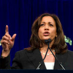 Kamala’s Step-Kid Loses It: Screeches Deranged ICE Rant Woman speaking passionately at a podium, gesturing upward.