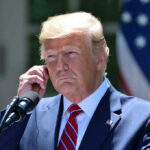 TRUMP Axes 66 Global Organizations Overnight Man in a suit adjusting an earpiece.