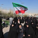Iran Protests EXPLODE – Regime on the Brink! Group of women in black attire marching with an Iranian flag