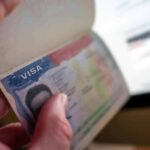 75 Countries FROZEN Out – Visa Chaos Erupts A hand holding an open passport displaying a visa page