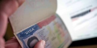 A hand holding an open passport displaying a visa page