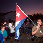 A group of people participating in a protest march holding a Cuban flag