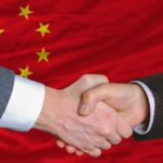 Canada Submits to China – Hails the “New World Order” Two hands shaking in front of the Chinese flag