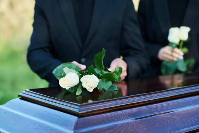 People placing white roses on a casket.