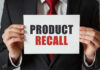 Product Recall sign held by person in suit.