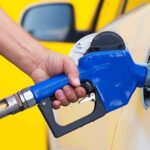 A person refueling a car at a gas station with a blue nozzle