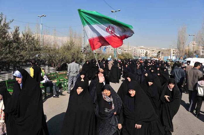 Group of women in black attire marching with an Iranian flag