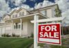 A suburban house with a For Sale sign in the front yard