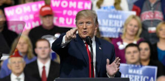 Person speaking at rally with crowd behind podium