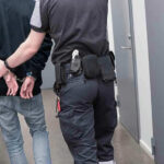 Officer escorting handcuffed person down hallway.