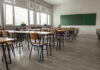 SICKO Teacher Forces Boy To Urinate In Class Empty classroom with desks, chairs, windows, and chalkboard.