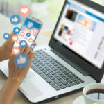 Person using smartphone and laptop with social media icons.