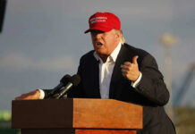 Person speaking at a podium wearing a red hat.