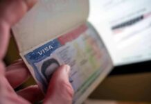 A hand holding an open passport displaying a visa page