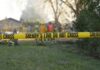 Yellow police tape marking a restricted area at a fire scene with firefighters in the background