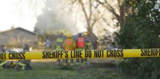 Yellow police tape marking a restricted area at a fire scene with firefighters in the background