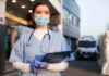 Nurse FIRED – Vowed To Not Treat Conservatives! Nurse in scrubs and mask outside hospital holding clipboard.