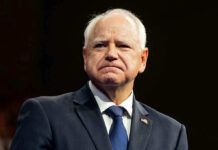 Tim Walz Pardons WORST of the WORST Illegal! Man in suit with a U.S. flag pin.
