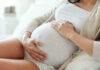 ALL Pregnant Travelers Need THIS For U.S Entry! Pregnant woman holding her belly, sitting comfortably.
